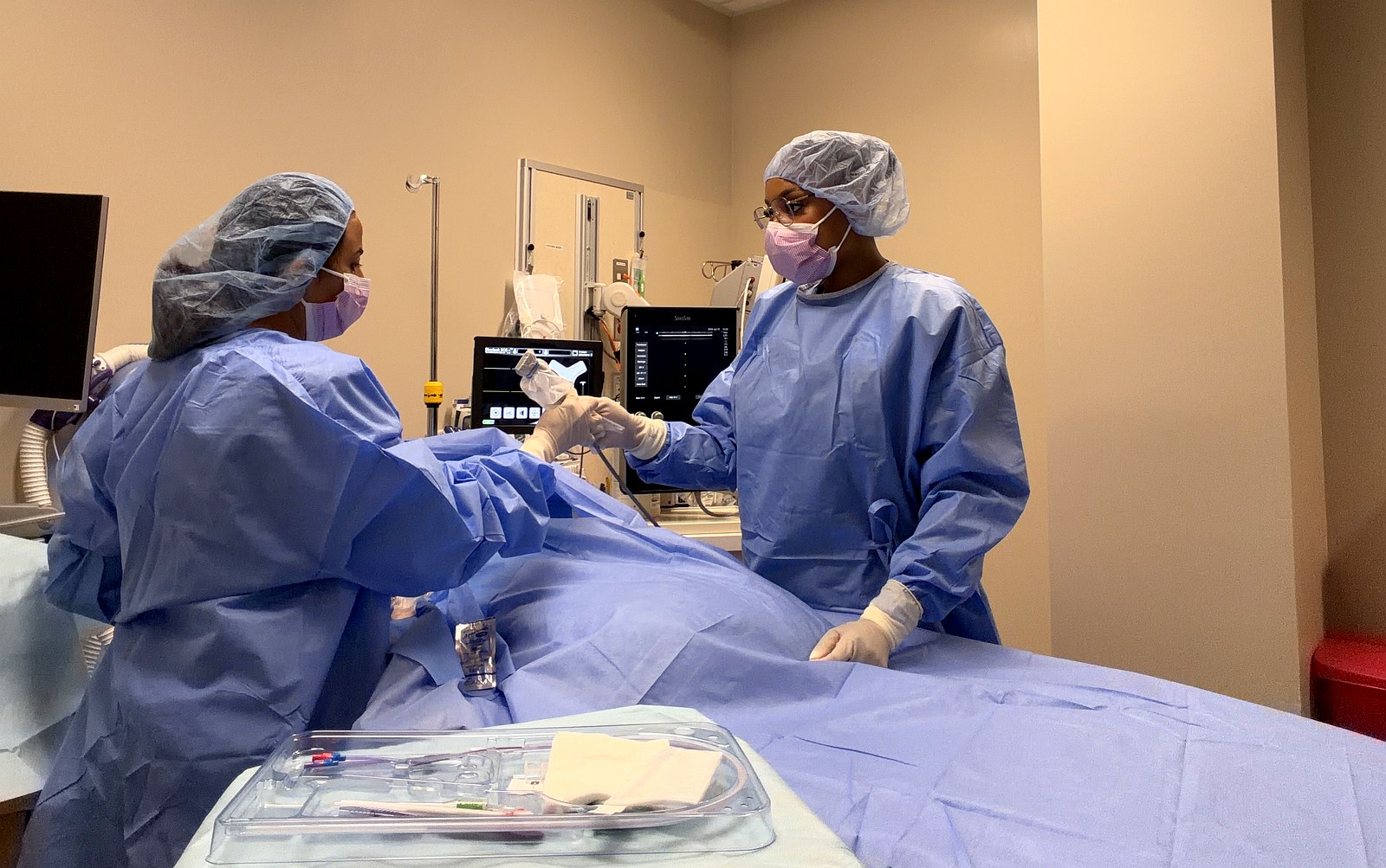 Urvashi and Tiara in sterile gowns performing PICC procedure together